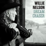 Side-profile of an elderly man with a cowboy hat and guitar, gazing out a window; poster to the right reads 'WILLIE NELSON DREAM CHASER'.