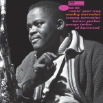 Black-and-white close-up of a jazz saxophonist on stage, instrument visible on the left and a cozy sweater collar seen in the foreground.